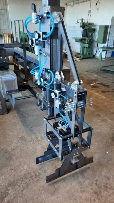 Maschinenteil mit Robotergreifer und blauen pneumatischen Schläuchen in einer Werkstatt.